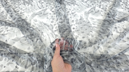 Tulle transparent cu desen gri și negru ridicat în mână, cu fundal vizibil prin rețeaua fină