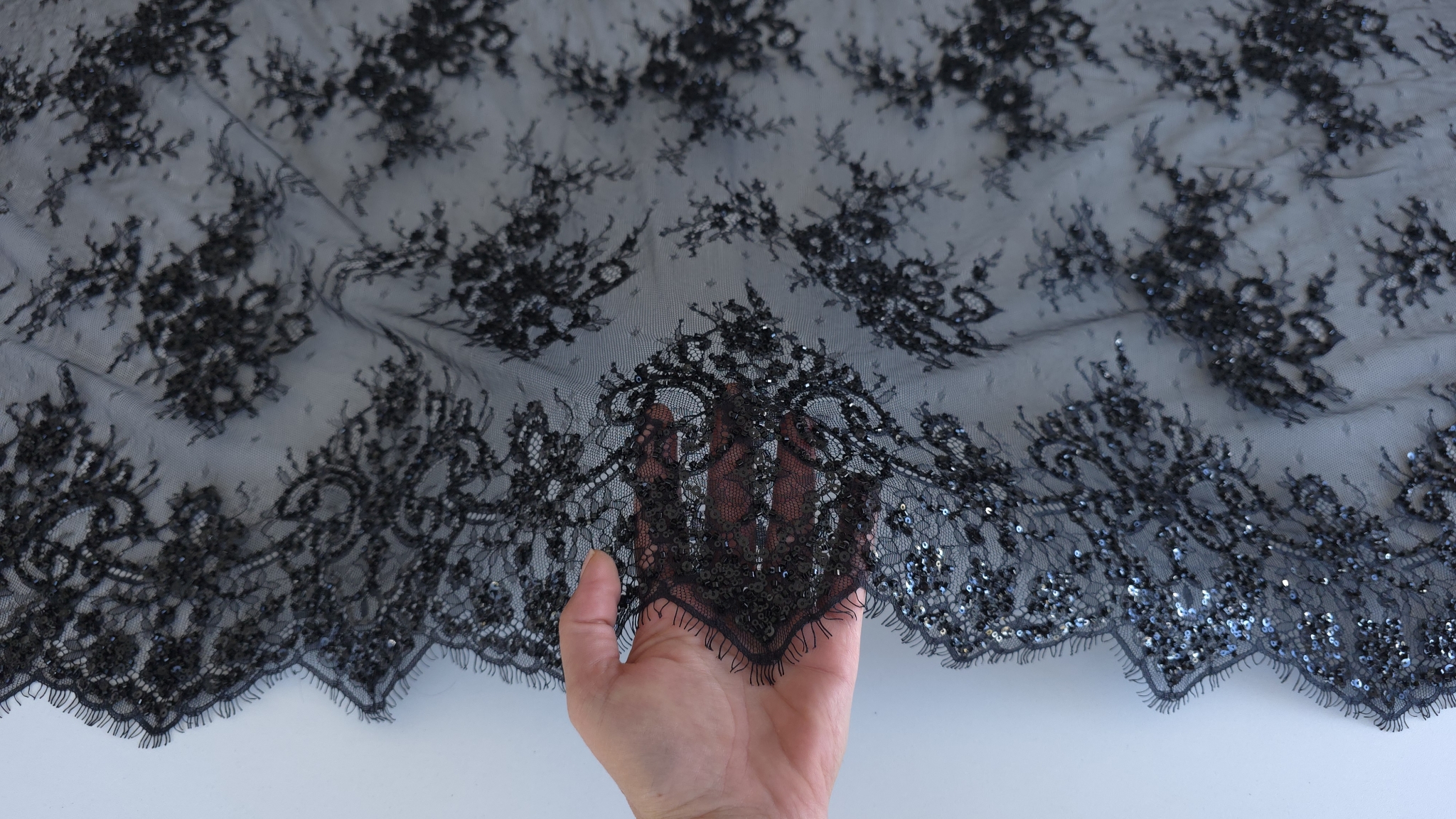 Dantela tip chantilly neagra accesorizata cu margelute ținută în mână, cu banda festonată în jos