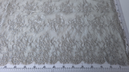 Broderie florală argintie pe fond dantelat transparent, măsurată cu riglă gradată pe suprafață plană