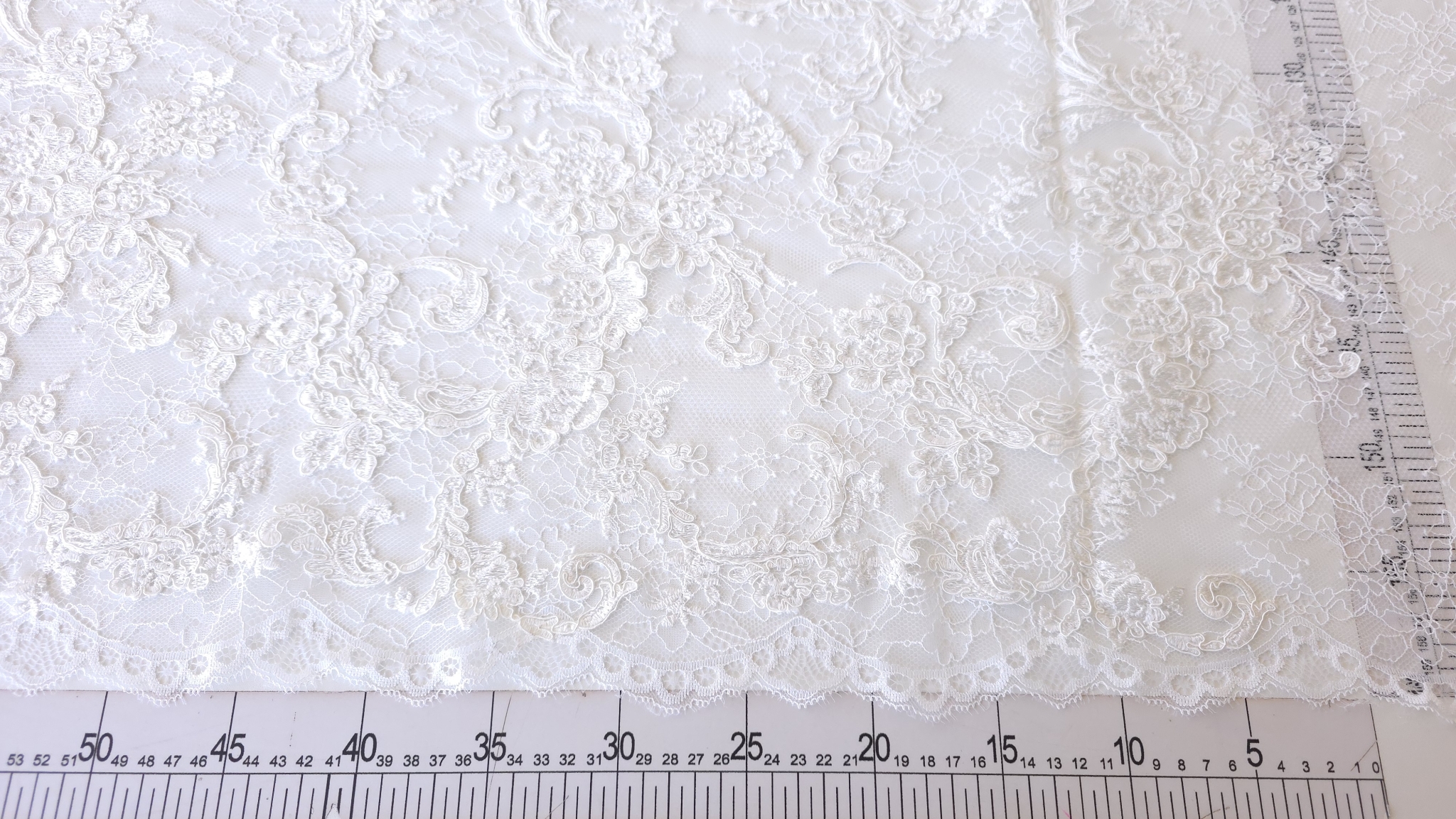Dantela tip chantilly rebrode off white întinsă pe masă și măsurată cu riglă