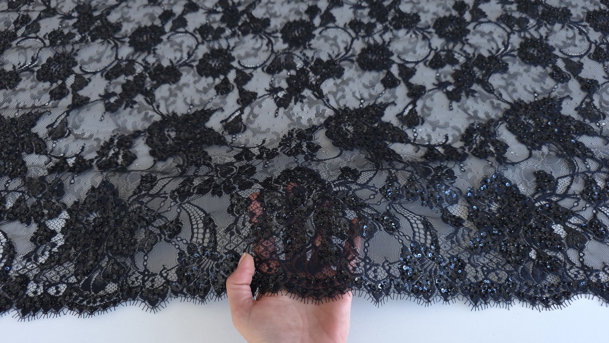 Dantela tip chantilly neagra accesorizata cu micropaiete ținută în mână