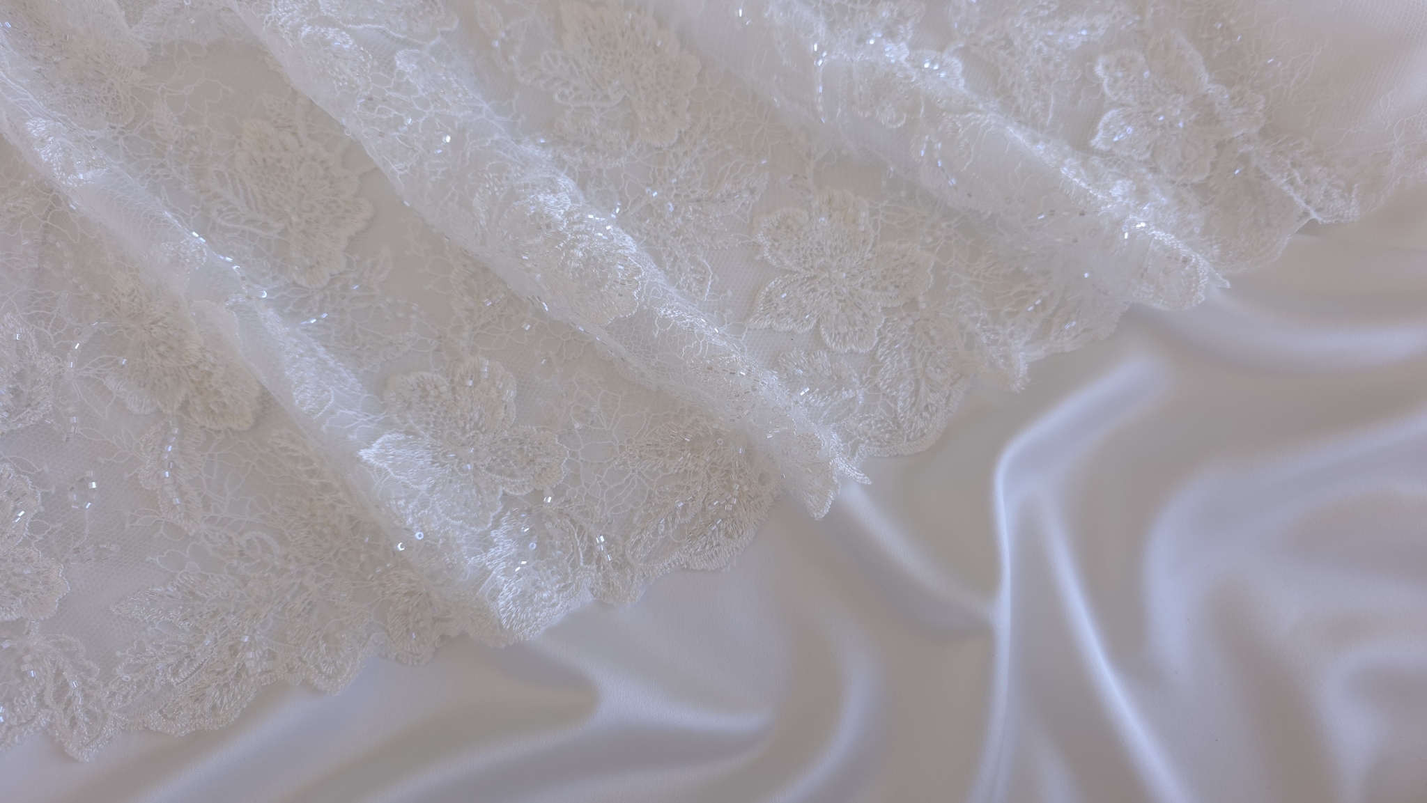 Dantelă off white cu flori brodate așezată peste căptușeală albă satinată