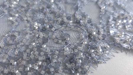 Detaliu macro al broderiei cu mărgeluțe gri lăptos, paiete translucide și fir în nuanță bleu gri
