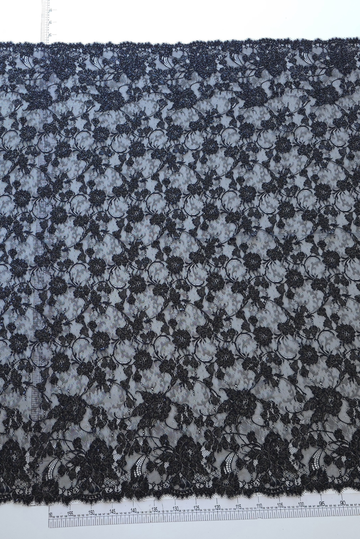 Dantelă florală neagră desfășurată pe masă, cu bordură pe ambele laturi