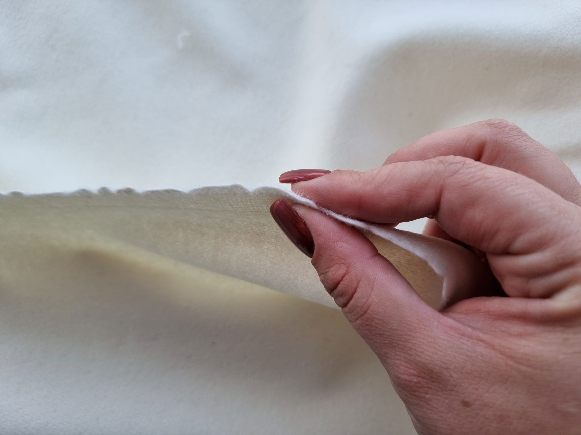 Marginea unui material ivoire ținut în mână, cu grosime medie și fața pufoasă