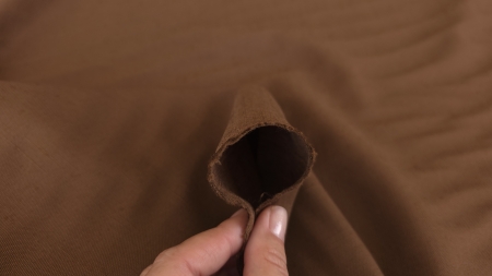 Marginea materialului maro deschis ținută între degete, rulată ușor