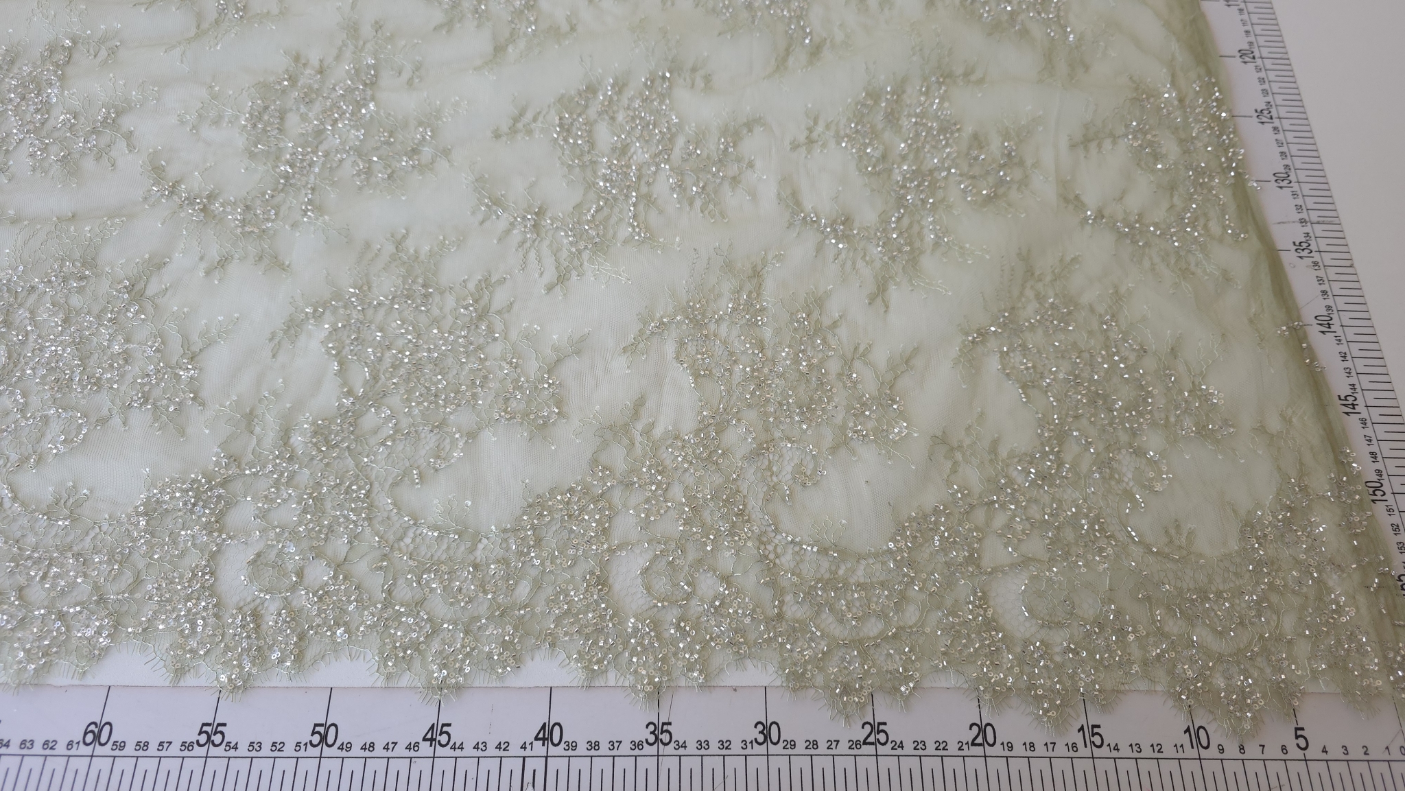 Colț de material verde deschis cu broderie densă, poziționat între două rigle