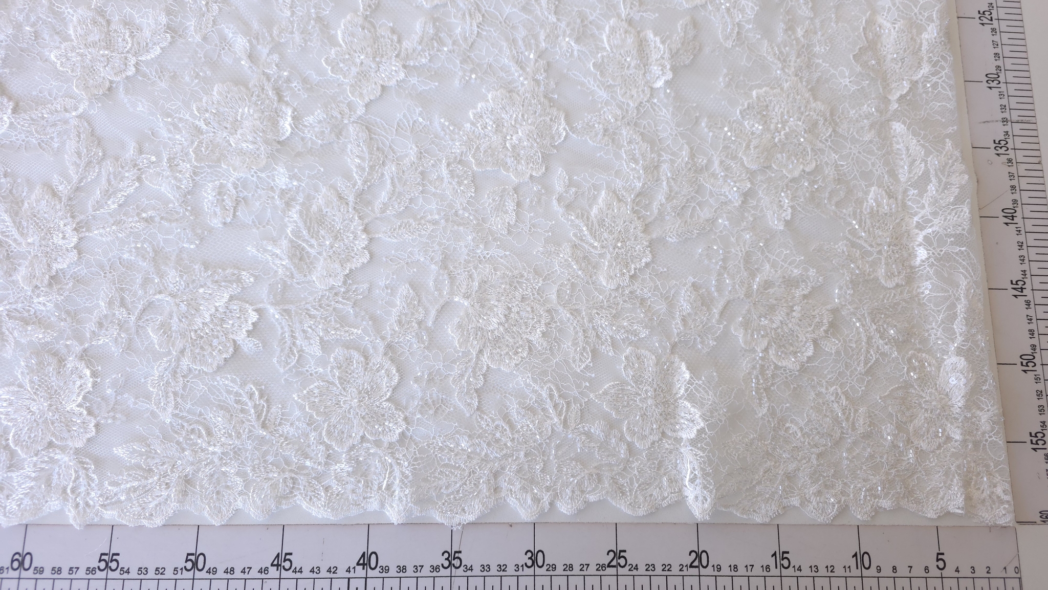 Panou de material off white cu flori brodate mari, poziționat pe rigla de croitorie