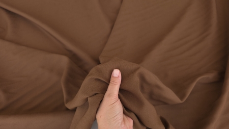Material maro deschis strâns în mână, cu pliuri moi