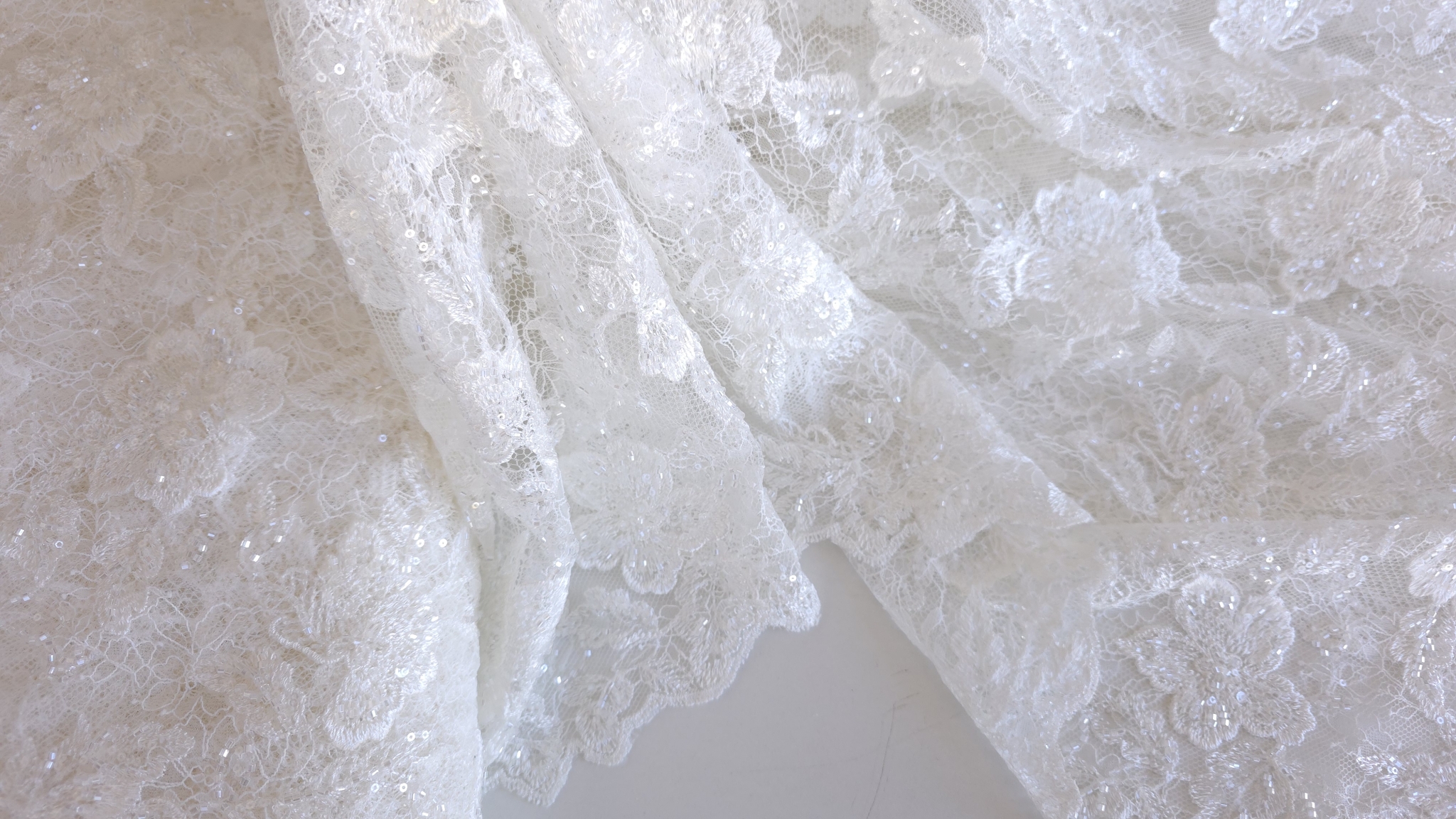 Material off white care coboară în pliuri lungi, cu sclipici mărunt pe petale
